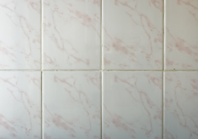 white ceramic wall tiles featuring a subtle light pink marble texture. The tiles are arranged in a grid with visible grout lines.